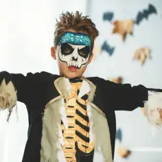 Chłopiec w makijażu czaszki i stroju szkieletu, idealny pomysł na to, jak zrobić strój zombie dla dziecka na Halloween.