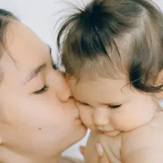 Czułe pocałunki mamy, gdy niemowlakowi rosną włosy. Delikatne kosmyki dziecka kontrastują z ciemnymi włosami matki.