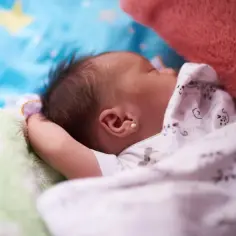 Śpiące tygodniowe dziecko, otulone kocykiem w gwiazdki. Widok z boku, skupiony na uchu z maleńką złotą kolczykiem.