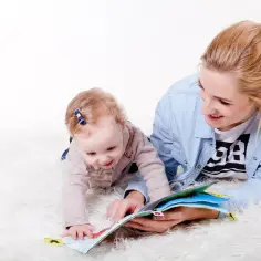 Mama czyta książeczkę dziecku, które raczkuje. Czas na wspólną zabawę, zanim pójdziemy do żłobka.