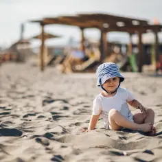 Uroczy maluch w kapelusiku na plaży. Idealne miejsce, gdzie na wakacje z rocznym dzieckiem.