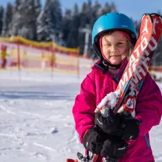 Mała narciarka z nartami w rękach, gotowa na zimowe szaleństwo. Idealne miejsce, gdzie na narty z dzieckiem w Polsce.