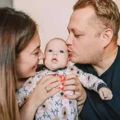 Mama i tata całują swoje maleństwo. Świat widziany oczami dwutygodniowego dziecka: rozmyte twarze, ciepło i miłość.
