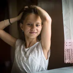 Uśmiechnięta dziewczynka z rękami we włosach. Czas, kiedy dziewczynki rosną najszybciej, pełen uroku i niewinności.
