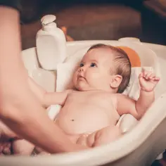 Delikatne kąpanie niemowlęcia w wanience. Rodzic ostrożnie myje dziecko, zastanawiając się, czy kąpać niemowlę z gorączką.