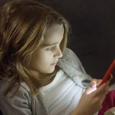 Dziewczynka z telefonem w dłoni, być może szuka informacji, jak wylogować dziecko z Family Link.