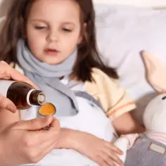 Dziecko w łóżku, mama podaje lek na łyżeczce. Ważne jest, jak dawkowac leki przeciwgorączkowe dziecku, by szybko poczuło ulgę.