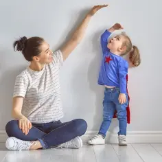 Mama mierzy, ile dziecko rosnie w rok. Mała superbohaterka próbuje sięgnąć jak najwyżej.