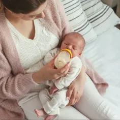 Mama karmi butelką śpiącego noworodka. Ile pieluch dziennie dla noworodka? To pytanie nurtuje wiele młodych rodziców.