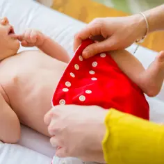 Ręce zapinają czerwoną pieluchę tetrową na niemowlaku. To praktyczny sposób, jak prać pieluchy tetrowe.