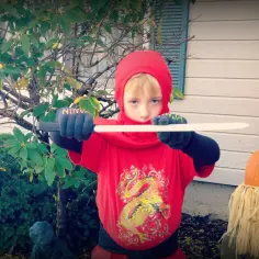 Chłopiec w czerwonym stroju ninja z mieczem, gotowy do akcji. To świetny pomysł, jak zrobić strój ninja na Halloween!