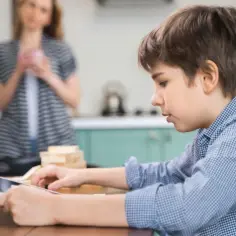 Chłopiec gra na tablecie, podczas gdy mama w tle zastanawia się, jak usunąć telefon z Family Link.