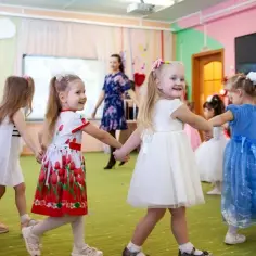 Dzieci w przedszkolu, tańczą w kółku. Ile lat się chodzi do przedszkola? Zwykle 3-6 lat, jak te uśmiechnięte maluchy.