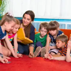 Nauczycielka czyta książkę grupie dzieci. W przedszkolu jest jedna opiekunka na siedmioro dzieci.