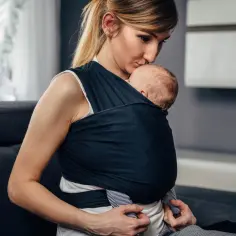 Mama czule całuje dziecko otulone w chustę. Pokazano, jak wiązać chustę do noszenia dziecka, tworząc bezpieczne i bliskie więzi.