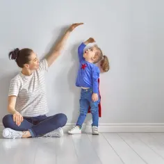 Mama mierzy, ile wzrostu ma roczna dziewczynka, która ubrana jest jak superbohaterka.