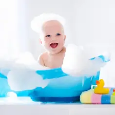 Uśmiechnięte dziecko w pianie w niebieskiej wanience. Ciekawi Cię, jak szybko rosną włosy u dzieci?