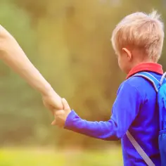 Mały chłopiec z niebieskim plecakiem, trzymający mamę za rękę, gdy rekrutacja do przedszkoli nabiera tempa.