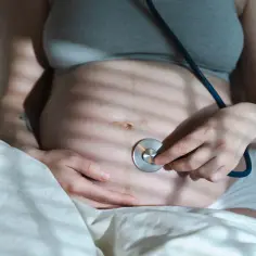 Kobieta z ciążowym brzuchem słucha stetoskopem, zastanawiając się, ile powinno być ruchów dziecka na godzinę.