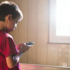 Chłopiec w czerwonej koszulce trzyma smartfon. Może szukać informacji, jak odblokować aplikacje w Family Link, gdy rodzic ustawił ograniczenia.