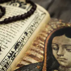 Różaniec na otwartej księdze z wizerunkiem Matki Boskiej. Wybór różańca na roczek to symboliczne powierzenie dziecka opiece Maryi.