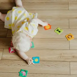 Dziecko leży na brzuchu, bawiąc się puzzlami ze zwierzątkami. Czy dziecko może spać na brzuchu? To pytanie nurtuje wielu rodziców.