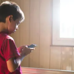 Chłopiec w czerwonej koszulce trzyma smartfon. Może szukać informacji, jak odblokować aplikacje w Family Link, gdy rodzic ustawił ograniczenia.