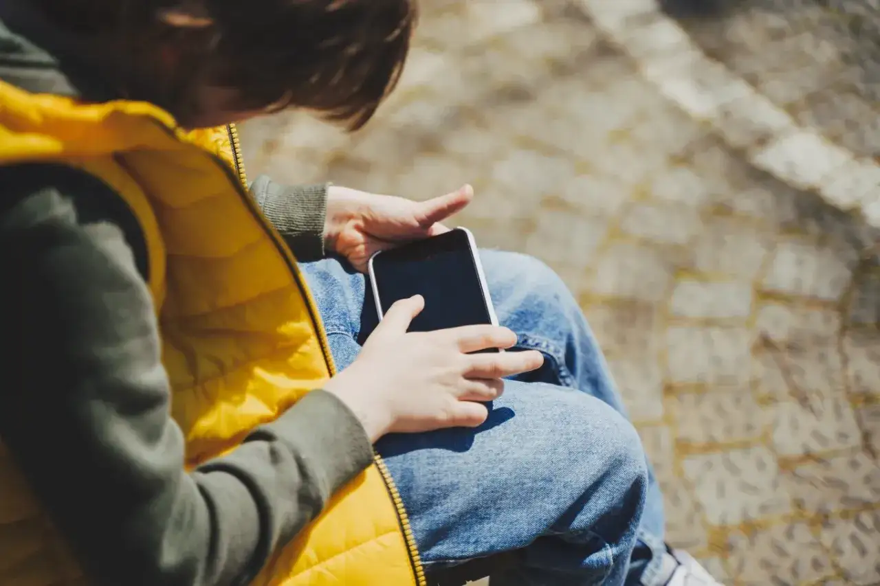 Dziecko w żółtej kamizelce próbuje dowiedzieć się, jak usunąć kontrolę rodzicielską na telefonie dziecka.