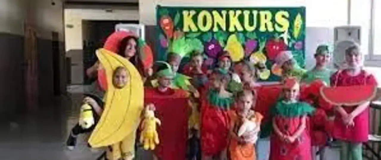 Dzieci w strojach warzyw i owoców, w tym strój banana i jabłka, pozują do zdjęcia na tle napisu 