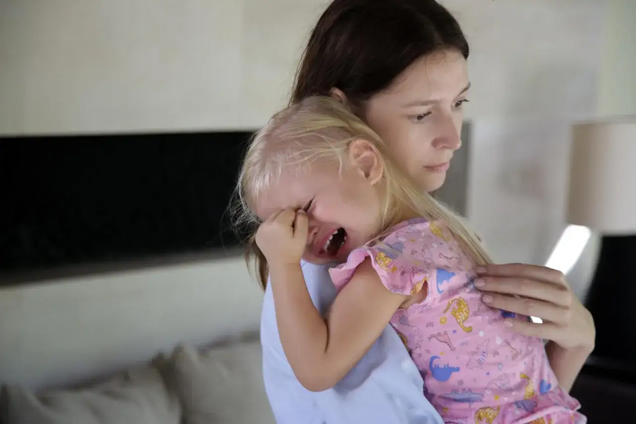Smutna dziewczynka płacze na ramieniu mamy. Czy to trudny początek, gdy zastanawiamy się, ile trwa adaptacja w przedszkolu?