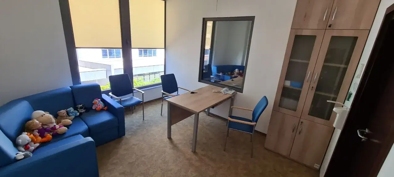 Pokój z niebieską kanapą pełną pluszaków, stołem i krzesłami. Miejsce, gdzie dziecko może zdecydować z którym rodzicem chce mieszkać.