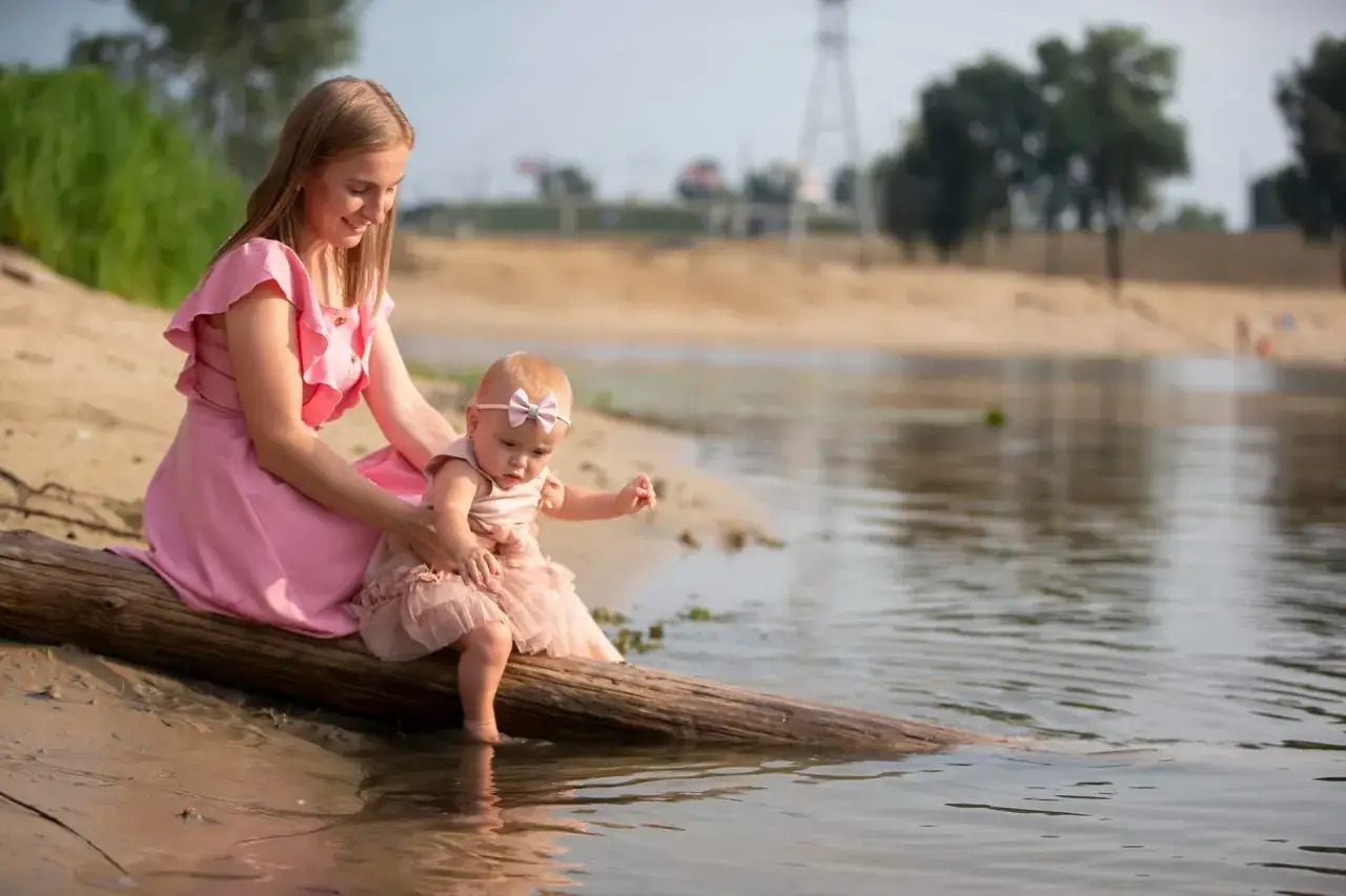 Mama i roczne dziecko siedzą na pniu przy rzece. Idealne miejsce, gdzie na wakacje z rocznym dzieckiem, by cieszyć się naturą.