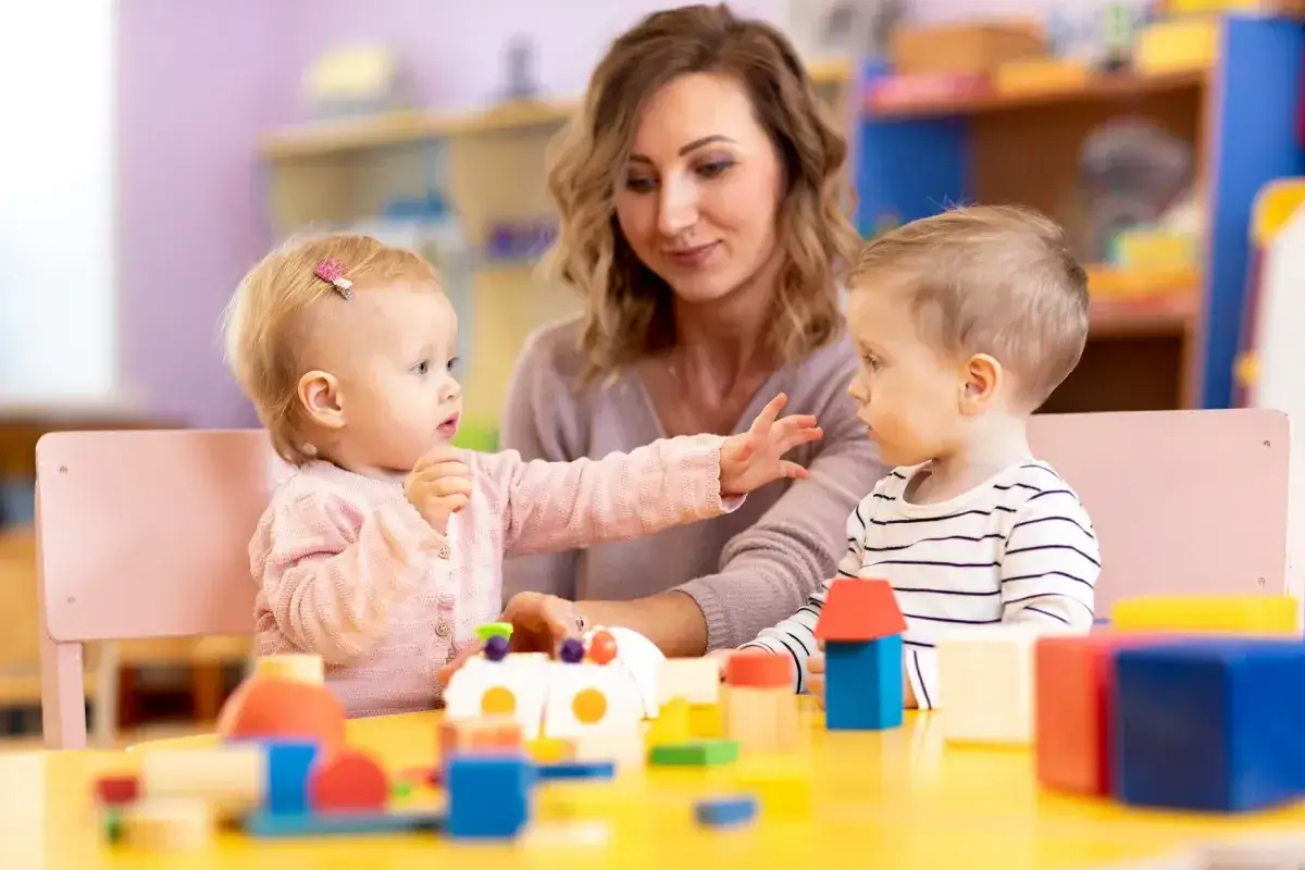 Dzieci bawią się klockami, a opiekunka czuwa. Zastanawiasz się, ile wcześniej zapisać dziecko do żłobka?