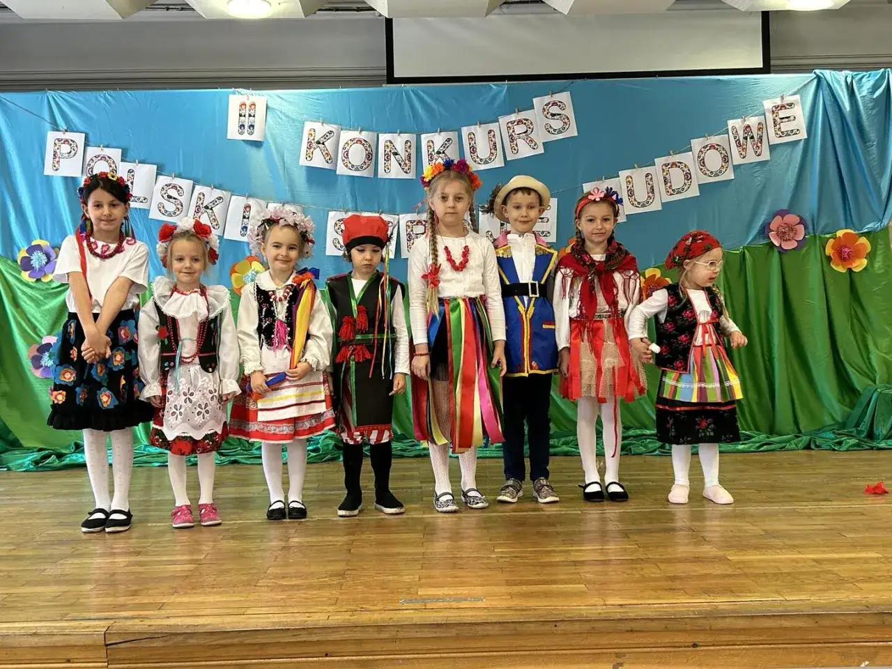 Dzieci w barwnych strojach ludowych prezentują się na scenie podczas konkursu.
