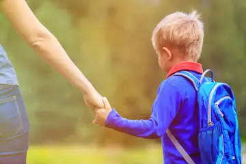 Mały chłopiec z niebieskim plecakiem, trzymający mamę za rękę, gdy rekrutacja do przedszkoli nabiera tempa.